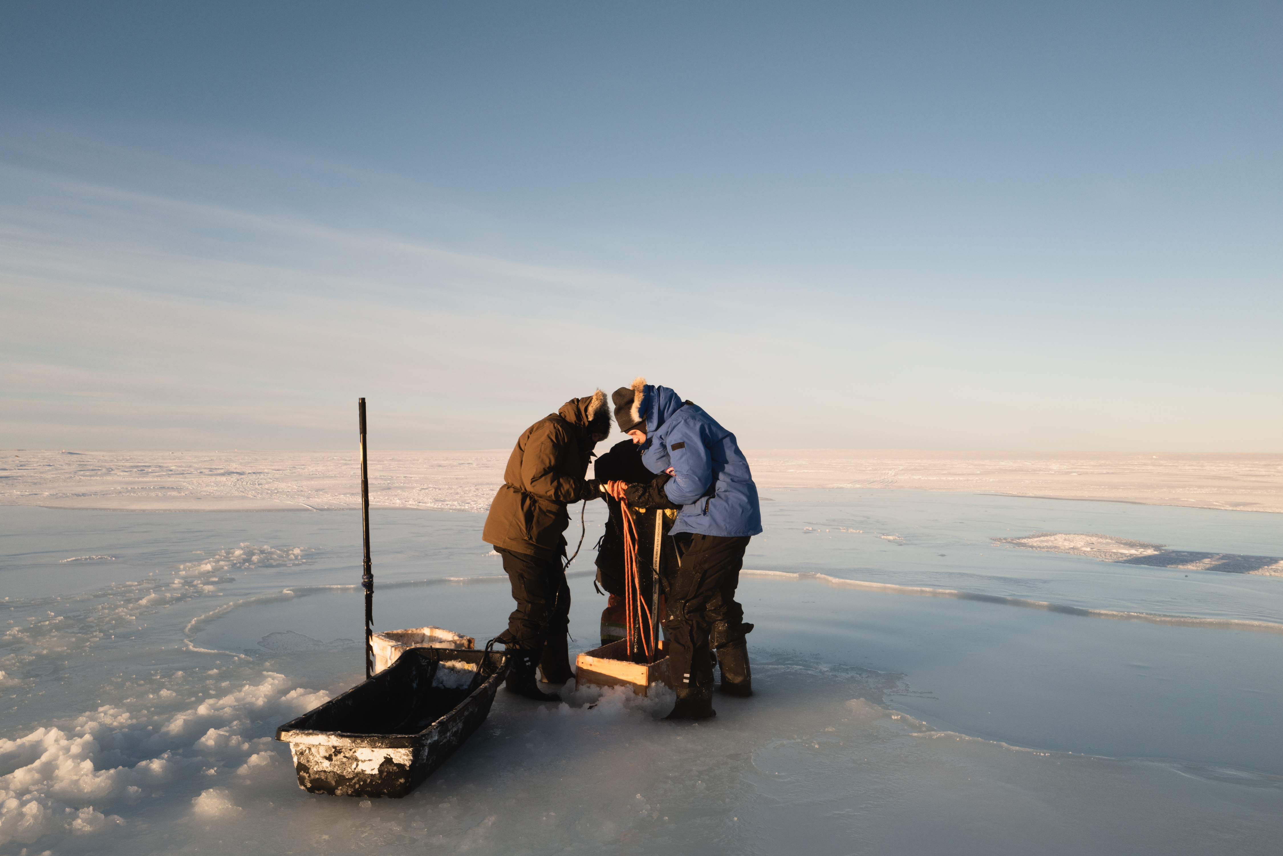 Photo of a team of people dressed in warm winter gear working on a water pump on an ice field in Canada