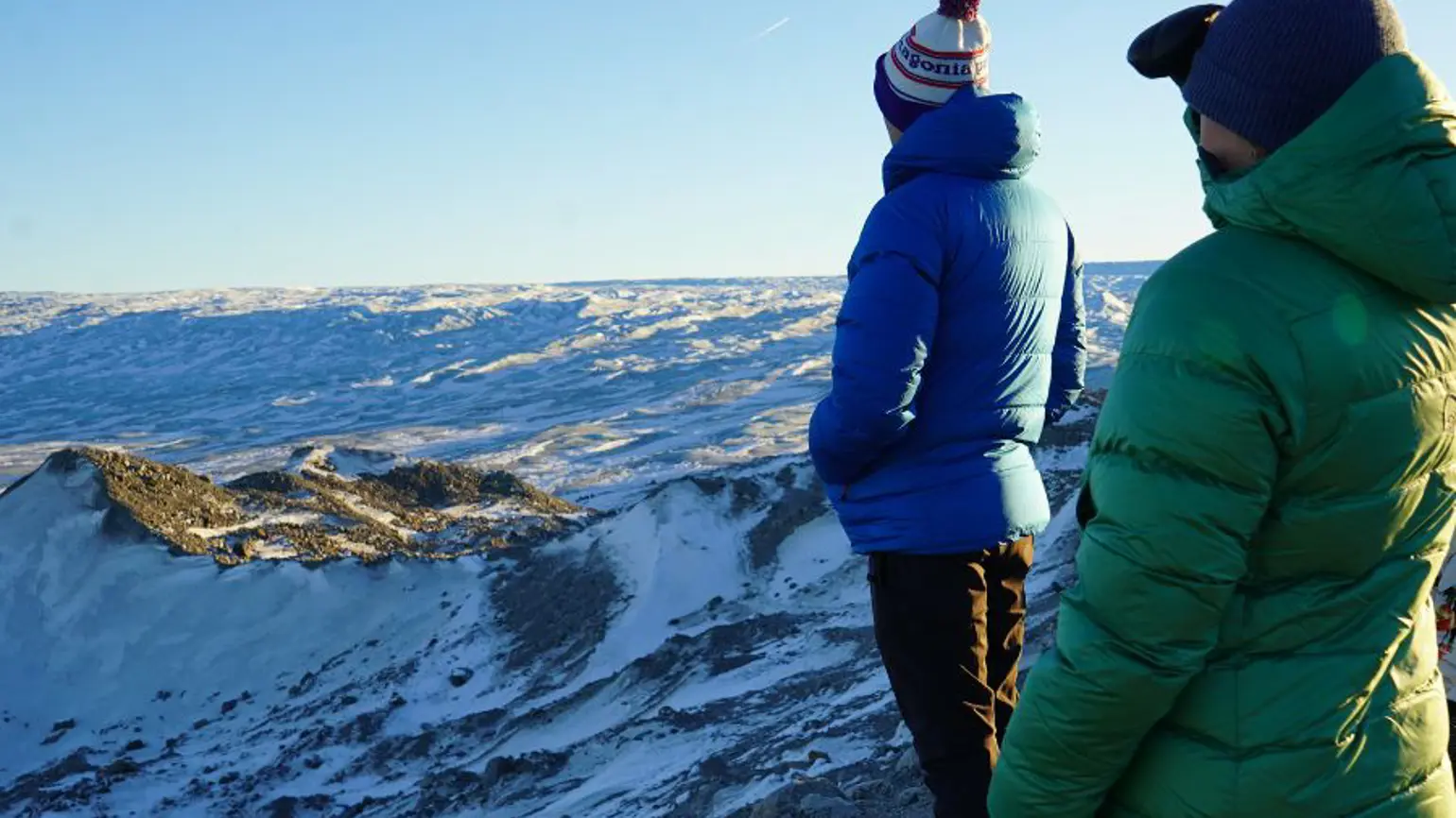 A photograph of two people in warm jackets looking out on a snowy landscape