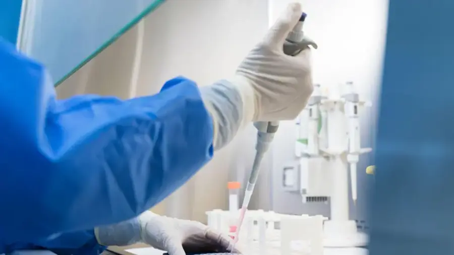 A scientist wearing blue scrubs using a pipette